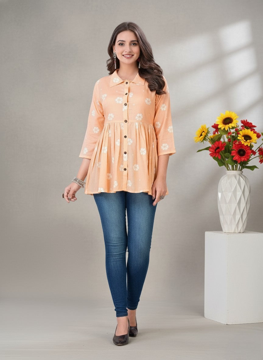 Woman wearing a peach floral blouse and blue jeans standing next to a vase of flowers.