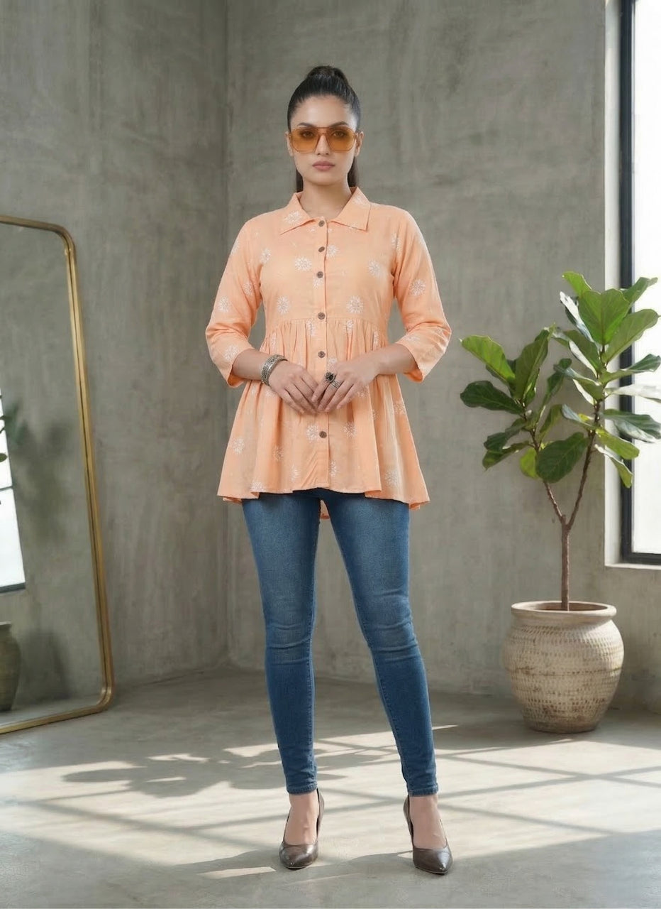 Woman wearing a peach blouse and blue jeans standing in a room with a plant and mirror.
