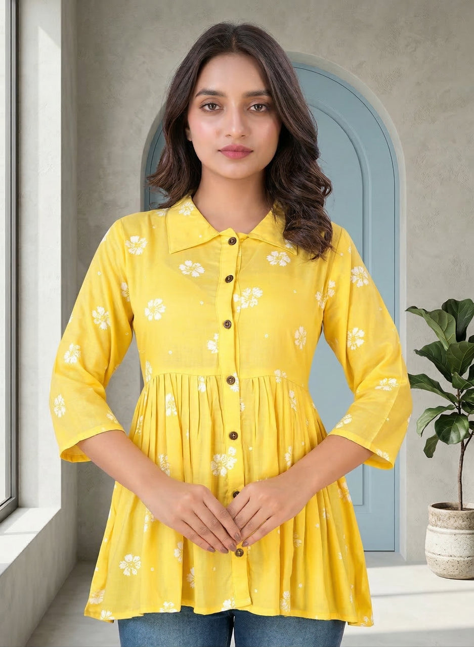 Woman wearing a yellow floral blouse standing indoors with a neutral background