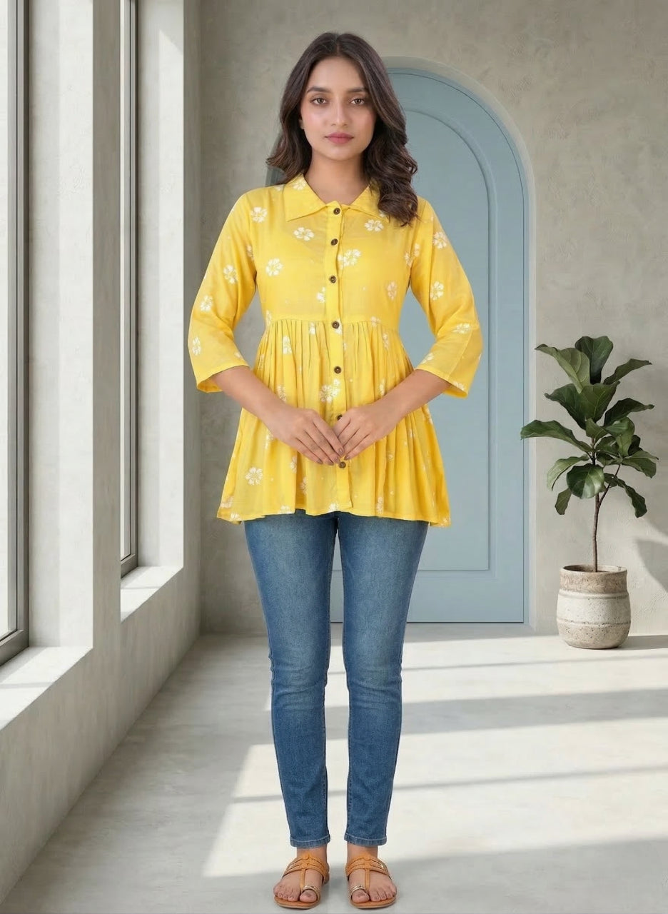 Woman wearing a yellow top and blue jeans standing in a room with a plant and window.