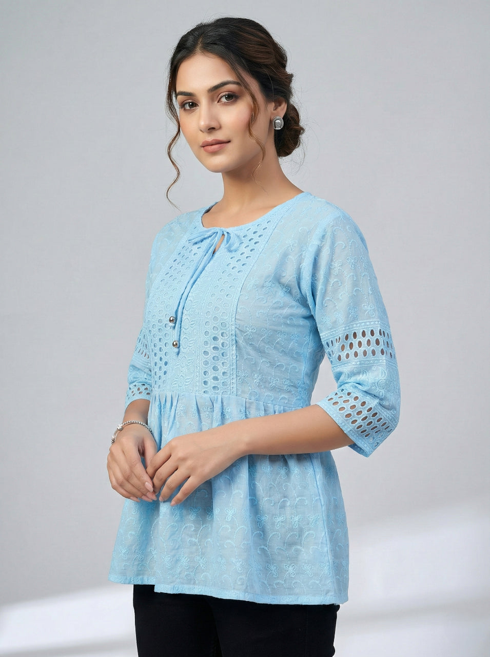 Woman wearing a light blue embroidered top against a plain background